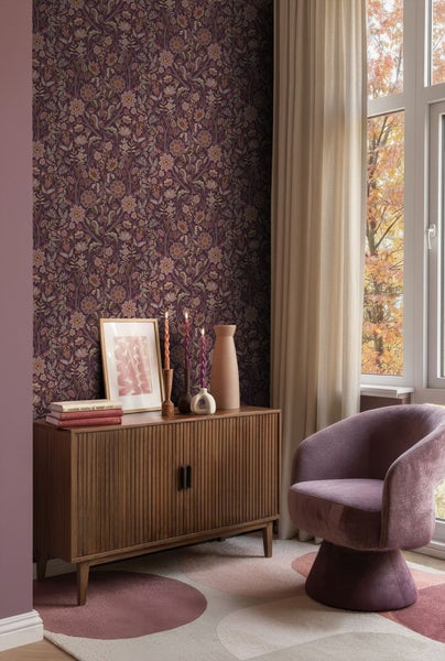 Wohnzimmer mit gemusterter Tapete, Holzkommode, Dekorationsgegenständen, Sessel und Teppich.