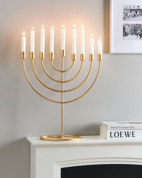 Goldfarbene Menorah aus Metall mit neun brennenden weißen Kerzen auf einem Kaminsims.