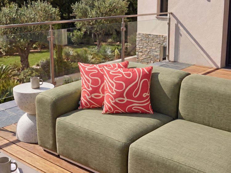 Zwei dekorative Zierkissen mit geschwungenem Muster auf einem modernen Lounge Sofa auf einer sonnigen Terrasse im Freien.