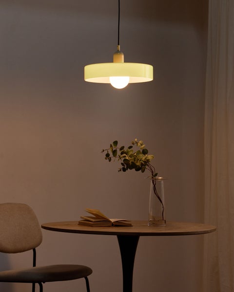 Pendelleuchte über einem runden Holztisch mit Stuhl, Buch und Vase in einem schlicht eingerichteten Raum.