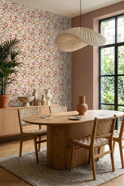 Wand mit floral gemusterter Tapete, einem geformten Spiegel und einem Marmortisch mit dekorativen Vasen und einer Kerze.