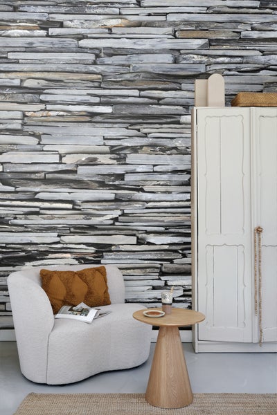 Wohnzimmer mit Steintapete, Sessel, Beistelltisch und Schrank.