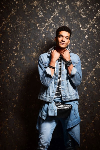 Mann mit Jeansjacke und Jeans vor einer gemusterten Wand