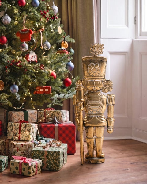 Goldene Nussknacker Figur als Weihnachtsdekoration neben einem geschmückten Weihnachtsbaum mit Geschenken auf einem Holzfußboden