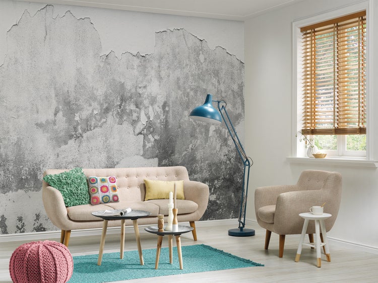 Fototapete in Betonoptik mit Putz-Struktur in einem hellen Wohnzimmer mit Sofa, Sessel, blauem Teppich und blauer Stehlampe.