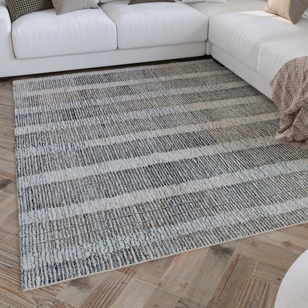 Gewebter Teppich mit Streifenmuster im Wohnzimmer vor einem hellen Sofa auf Holzparkett.