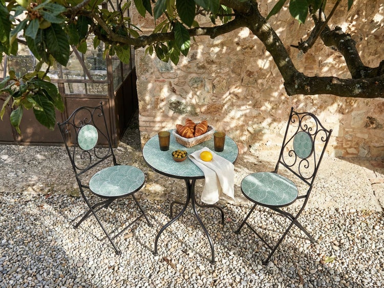 Gartenszene mit Bistrotisch und zwei Bistro Stühlen auf Kiesboden, inklusive Speisen und Getränke