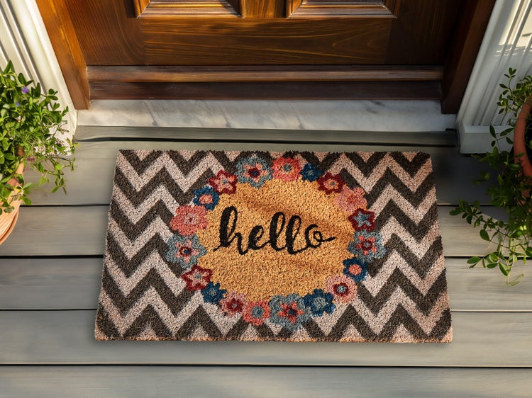 Rechteckige Kokos-Fussmatte mit Zickzack-Muster, Blumenkranz und dem Schriftzug hello vor einer Haustuer.