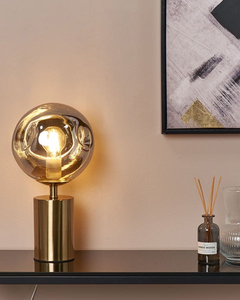 Dekorative Tischleuchte mit einem runden Lampenschirm aus Glas auf einem goldenen Sockel.