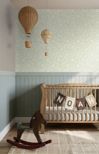 Kinderzimmer mit floral gemusterter Tapete, hellblauer Holzvertäfelung, einem hölzernen Gitterbett, einem Schaukelpferd und geflochtenen Heißluftballons.