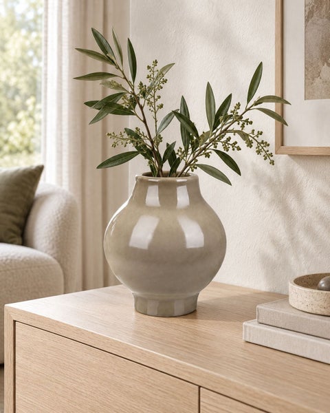 Dekorative bauchige Vase aus Keramik mit Olivenzweig auf einem Holztisch in einem Wohnzimmer.