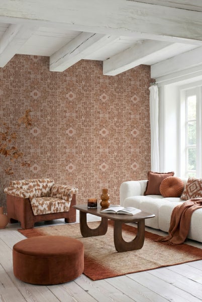 Mustertapete mit Ethno-Design in Terrakotta-Tönen in einem hellen Wohnzimmer mit weißem Sofa, Holzcouchtisch und Sessel.