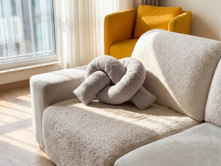 Modernes Knotenkissen aus Teddy-Fleece auf einem hellen Sofa in einem lichtdurchfluteten Wohnzimmer.