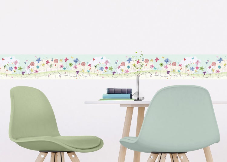 Selbstklebende Wandbordüre für das Kinderzimmer mit bunten Blumen und Schmetterlingen auf einer rosa Wand mit Giraffen-Plüschtier und Herzkissen.