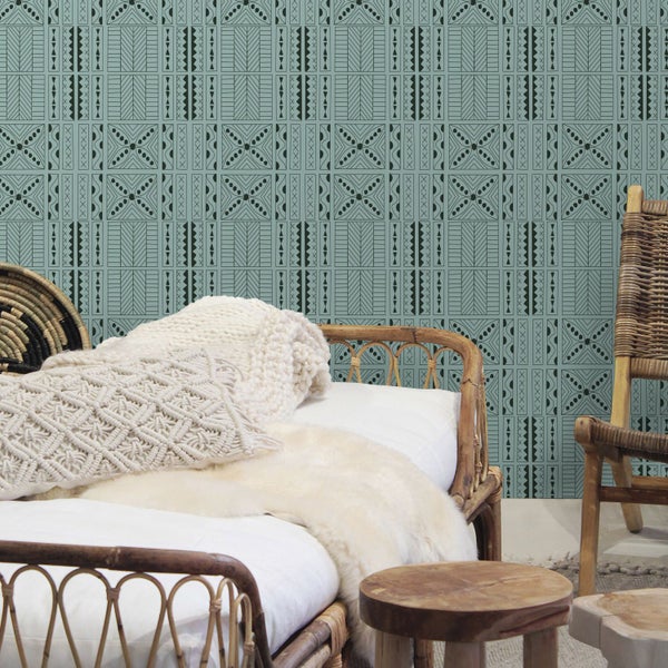 Schlafzimmer mit Rattanbett, Dekokissen und gemusterter Tapete für ein gemütliches Ambiente.