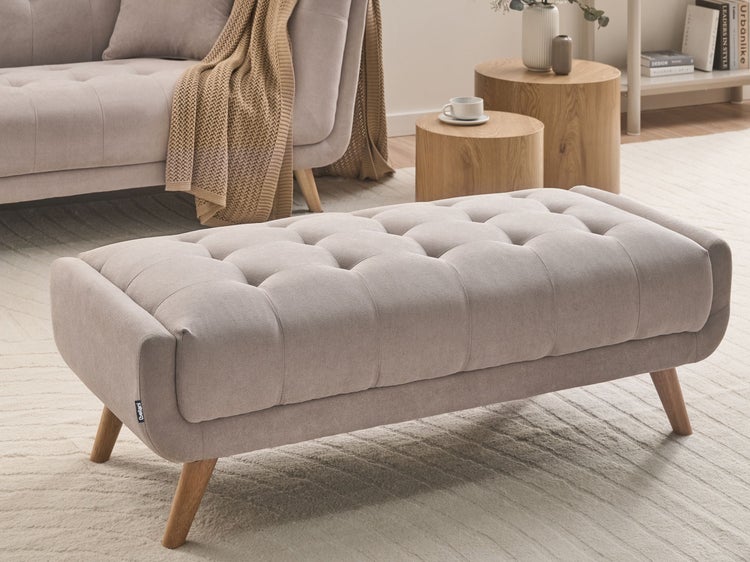 Gepolsterte Sitzbank mit Knopfheftung und Holzbeinen in einem hellen Wohnzimmer mit Sofa und runden Beistelltischen aus Holz.