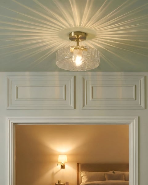 Deckenleuchte mit strukturiertem Glasschirm und Metallhalterung, die ein strahlenförmiges Lichtmuster an die Decke wirft.