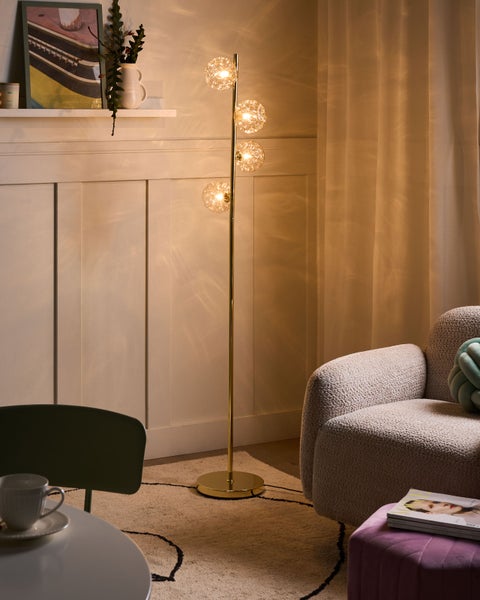 Stehlampe mit drei kugelförmigen Lampenschirmen und einem goldfarbenen Gestell in einem Wohnzimmer.