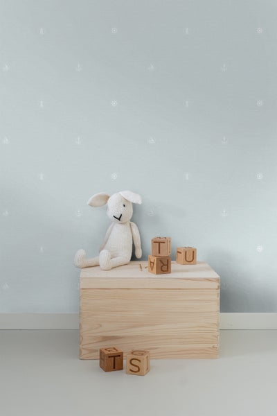 Szene mit hellblau gemusterter Tapete, Holzkiste, Stofftier und Spielwürfeln
