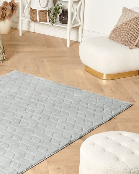 Heller Raum mit grauem Teppich mit geometrischem Muster, Sessel und Dekoration