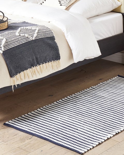 Gestreifter Webteppich auf Holzboden in einem hellen Schlafzimmer neben einem Bett mit Tagesdecke.