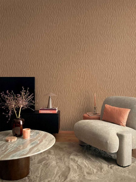 Wohnzimmer mit Vliestapete mit organischem Wellenmuster, kombiniert mit einem modernen Sessel, Marmortisch und dekorativen Wohnaccessoires.