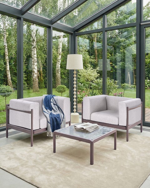 Moderner Wintergarten mit zwei Sesseln, einem quadratischen Couchtisch mit Glasplatte, einer Stehleuchte und einem Teppich.