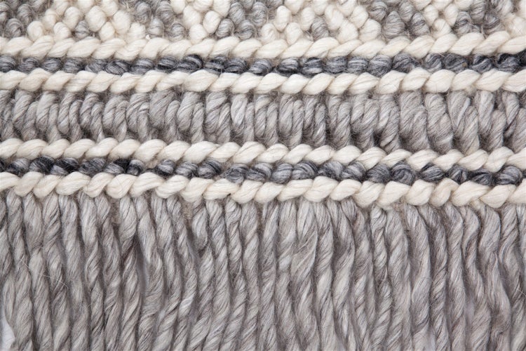 Detailaufnahme eines gewebten Wollteppichs mit verschiedenen Mustern, Strukturen und Fransen am Rand.