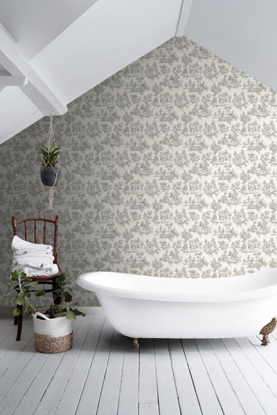Badezimmer mit freistehender Badewanne, Toile-de-Jouy-Tapete mit Waldmotiven, Holzstuhl mit Handtüchern und Zimmerpflanzen.