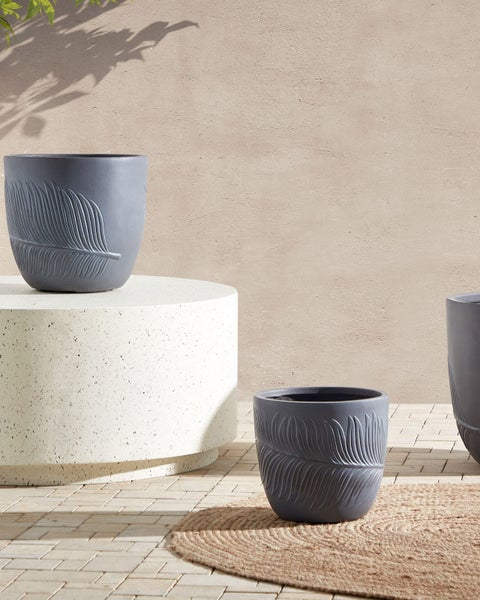 Drei graue Pflanzgefäße mit Federdesign auf einem Podest und einem Teppich