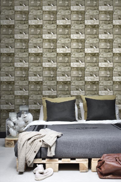 Bett mit dekorativer Tapete im Kofferdesign, gemütlichen Kissen und einer Tagesdecke auf einer Holzpalette.