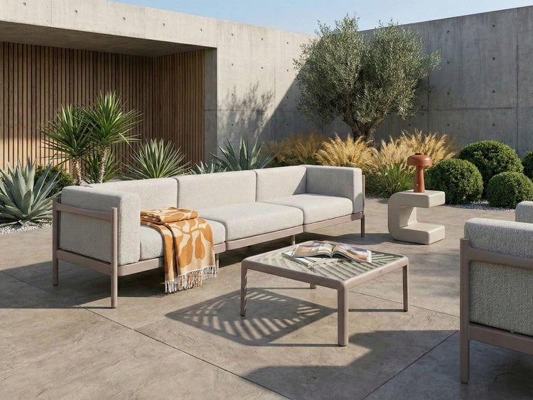 Moderne Gartenlounge mit Sofa, Sessel und Glastisch auf einer hellen Terrasse mit Betonwänden, Holzverkleidung und Pflanzen.