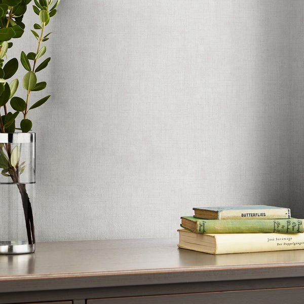Strukturierte Vliestapete vor einer Wand mit Vase und Büchern auf einem Sideboard im Wohnbereich.