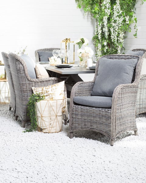 Gartenszene mit Rattansesseln, Esstisch und dekorativen Elementen für den Außenbereich