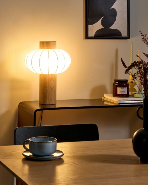 Szene mit einer Tischleuchte, einer Kommode, Dekorationsgegenständen und Geschirr auf einem Tisch.