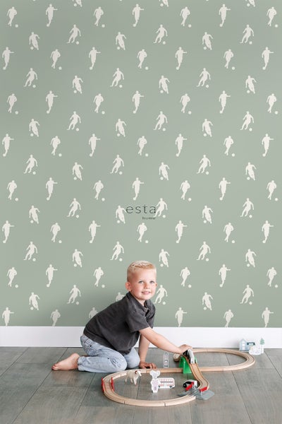 Kind spielt mit Spielzeug vor einer Wand mit Fußball Tapete.