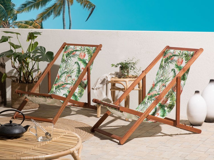 Szene mit zwei Holz-Deckchairs mit tropischem Muster, einem Beistelltisch, Pflanzen und dekorativen Vasen für den Außenbereich.