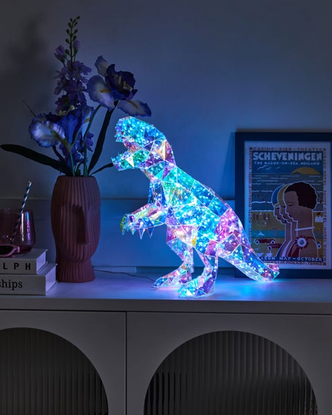 Dekoratives beleuchtetes Dinosaurierornament auf einem Sideboard mit Blumen und einem Poster
