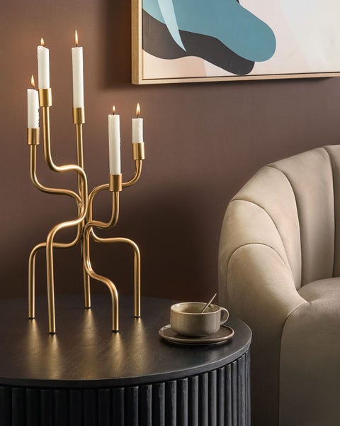 Dekorative Szene mit einem goldenen Kerzenständer mit fünf brennenden Kerzen auf einem schwarzen Tisch mit einer Tasse.