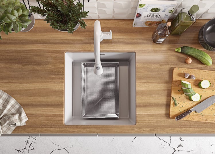 Küchenspüle mit Armatur, Schneidebrett, Gemüse und Kochbuch in einer hellen Küche.