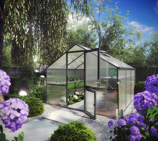 Gewächshaus mit schwarzem Metallrahmen und Hohlkammerplatten in einem hellen, gepflegten Garten mit Blumen und Kiesweg.