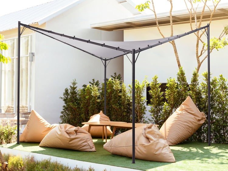 Moderner Pavillon mit dunkelgrauem Metallgestell und hellgrauem Stoffdach in einem Garten mit Sitzsäcken und Holztischen.