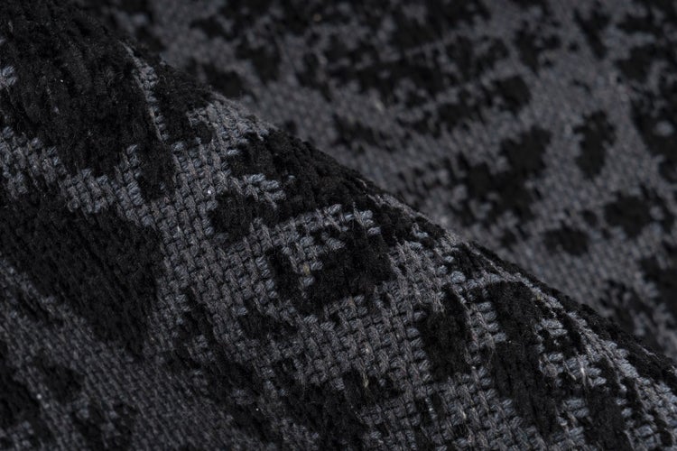 Gewebter Teppich mit dunklem abstraktem Muster und strukturierter Oberfläche.