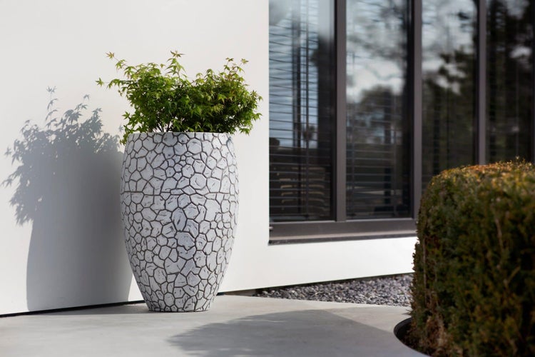Hoher Pflanzkübel mit Mosaikstein-Struktur und Pflanze auf einer modernen Terrasse.