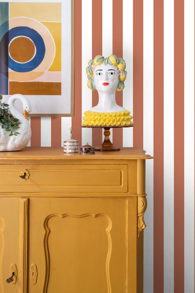 Dekoratives Arrangement mit Kommode, Ziergefäß, Kunst und Accessoires vor gestreifter Wand