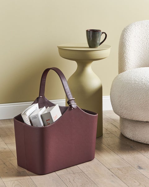 Dekorative Aufbewahrungstasche aus Stoff mit Tragegriffen, Tisch und Sessel im Hintergrund.