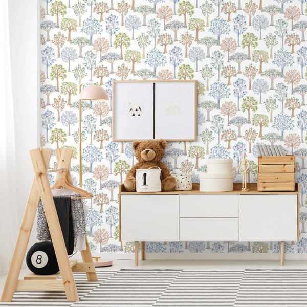 Helles Kinderzimmer mit Tapete mit Baummuster, einem Sideboard aus Holz und Weiß mit einem Teddybär sowie einem hölzernen Kleiderständer.