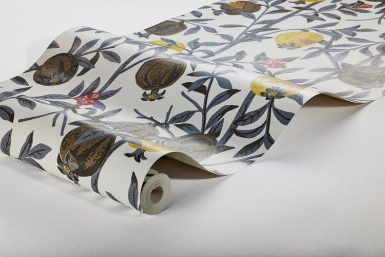 Szene mit einem gepolsterten Hocker, Büchern und einer dekorativen Tapete mit Pflanzenmotiven.