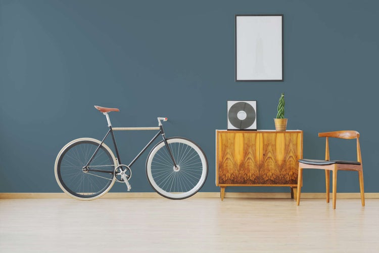 Modern eingerichtetes Zimmer mit Sideboard aus Holz, Holzstuhl und Fahrrad auf hellem Holzboden, organisierter und minimalistischer Stil.