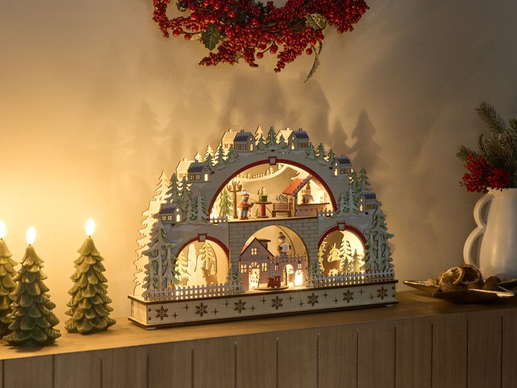 Dekorative Lichterbogen-Szene mit Weihnachtsmotiven, Figuren und warmem Licht auf einer Kommode.